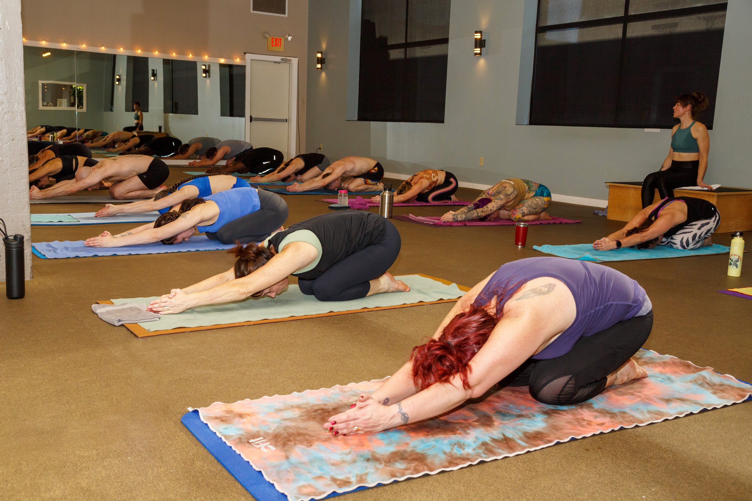 Full class resting in half tortoise pose, foreheads down on their mats in the heated studio